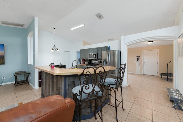 kitchen with stainless steel appliances, pendant lighting, light tile patterned floors, a chandelier, and lofted ceiling