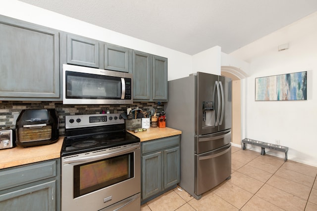 kitchen featuring decorative backsplash, stainless steel appliances, gray cabinetry, and light tile patterned flooring