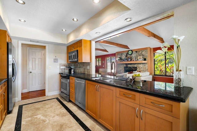 kitchen with sink, a fireplace, appliances with stainless steel finishes, tasteful backsplash, and beamed ceiling