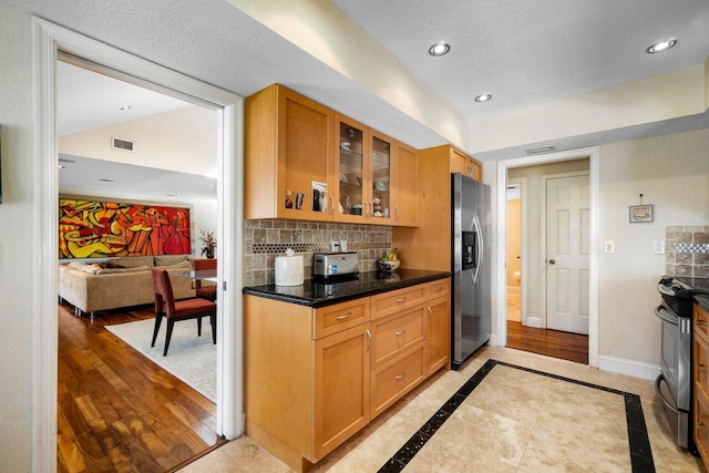 kitchen featuring appliances with stainless steel finishes, tasteful backsplash, a textured ceiling, dark stone countertops, and light hardwood / wood-style floors