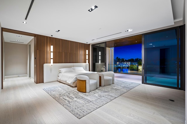 bedroom with wood walls, expansive windows, light hardwood / wood-style floors, and access to exterior