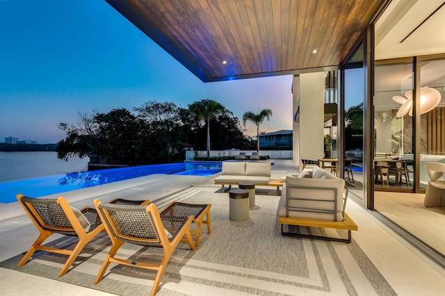 pool at dusk with an outdoor living space, a water view, and a patio