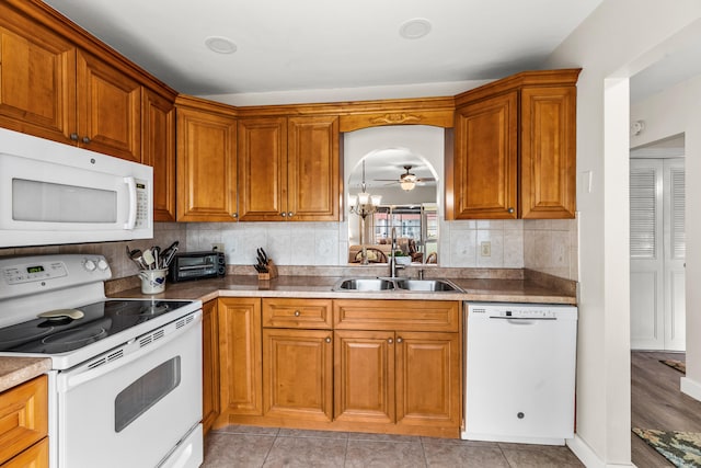 kitchen featuring sink, white appliances, decorative backsplash, light tile patterned floors, and ceiling fan with notable chandelier