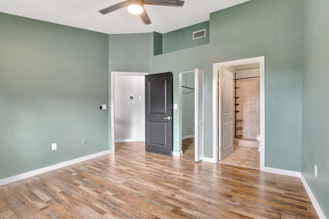 unfurnished bedroom featuring ensuite bathroom, light wood-type flooring, a towering ceiling, and ceiling fan