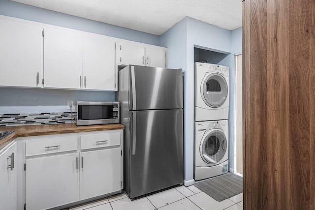 kitchen with white cabinetry, appliances with stainless steel finishes, a textured ceiling, light tile patterned floors, and stacked washer / drying machine