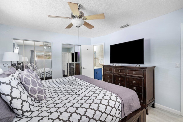 bedroom with ensuite bath, ceiling fan, a textured ceiling, multiple closets, and light hardwood / wood-style flooring