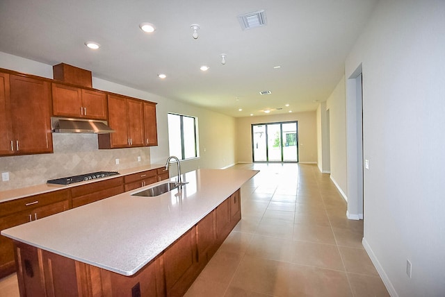 kitchen featuring sink, gas stovetop, backsplash, an island with sink, and light tile patterned flooring