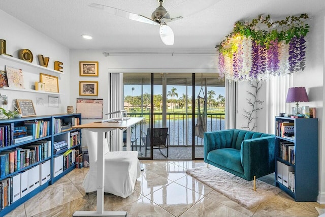 sitting room with a textured ceiling, a water view, and ceiling fan