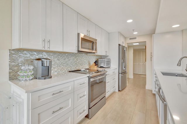 kitchen with appliances with stainless steel finishes, backsplash, light wood-type flooring, sink, and white cabinets