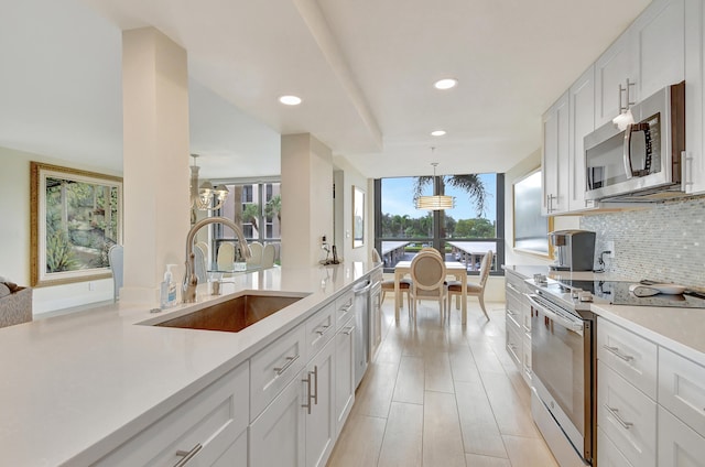 kitchen featuring pendant lighting, sink, light hardwood / wood-style flooring, appliances with stainless steel finishes, and white cabinetry