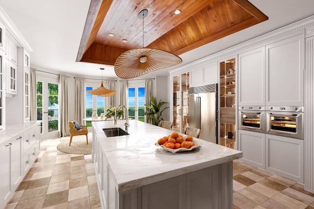 kitchen with stainless steel appliances, white cabinetry, an island with sink, and decorative light fixtures