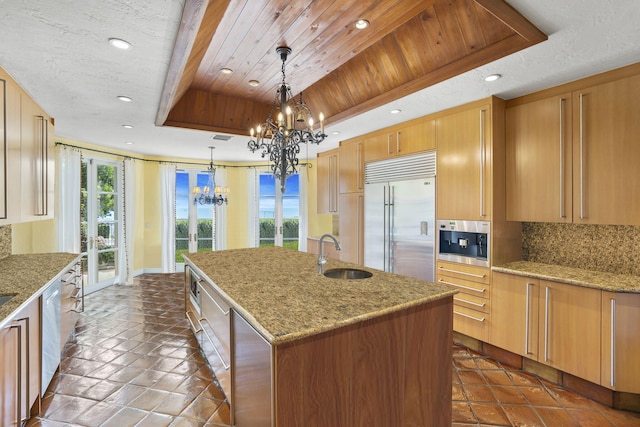 kitchen featuring stainless steel appliances, sink, decorative light fixtures, a raised ceiling, and a kitchen island with sink