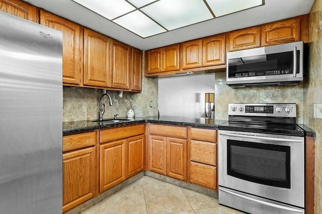 kitchen with sink, decorative backsplash, dark stone countertops, light tile patterned floors, and appliances with stainless steel finishes