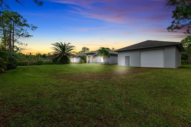 yard at dusk featuring a garage and an outbuilding