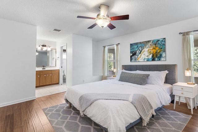 bedroom featuring sink, ceiling fan, light wood-type flooring, a textured ceiling, and connected bathroom