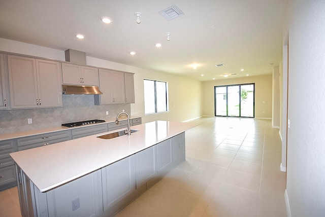 kitchen featuring backsplash, gray cabinetry, a wealth of natural light, and an island with sink