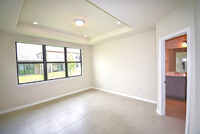 spare room with a raised ceiling, sink, and light tile patterned floors