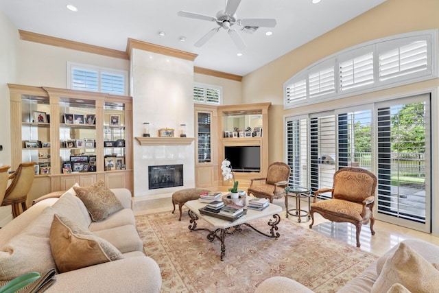 living room featuring a high ceiling, crown molding, ceiling fan, light tile patterned floors, and a large fireplace