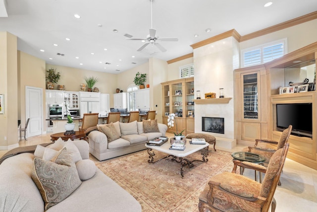 living room featuring a high ceiling, a large fireplace, ceiling fan, and crown molding