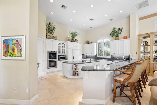 kitchen with kitchen peninsula, a kitchen breakfast bar, stainless steel double oven, white cabinets, and a center island