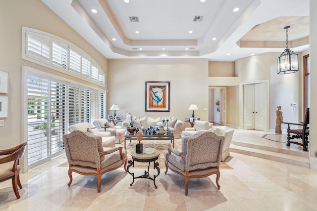 living room with a raised ceiling, a high ceiling, and a notable chandelier