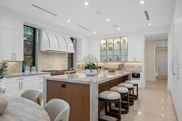 kitchen with a kitchen bar, white cabinetry, custom exhaust hood, and a center island