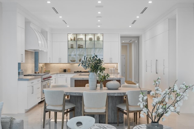 kitchen featuring custom exhaust hood, backsplash, a kitchen island, white cabinets, and high end stainless steel range oven