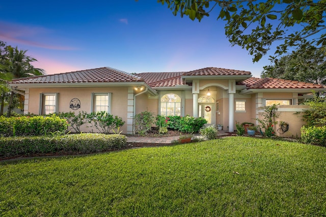 mediterranean / spanish house with stucco siding, a front lawn, and a tiled roof