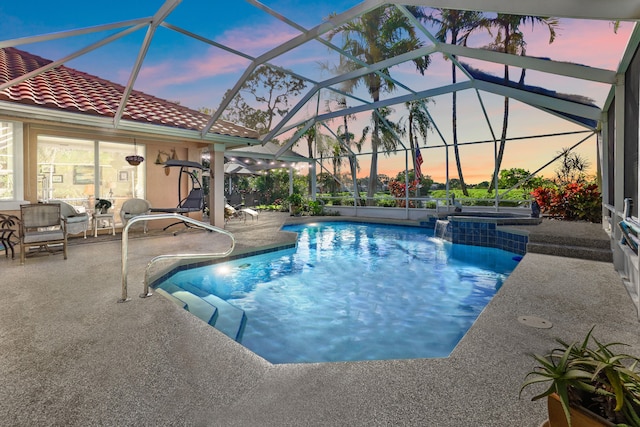 pool at dusk featuring glass enclosure and a patio