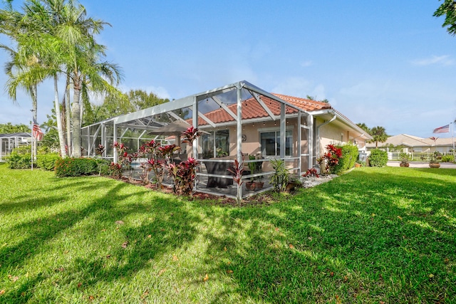 back of house with glass enclosure, a lawn, a tiled roof, and stucco siding