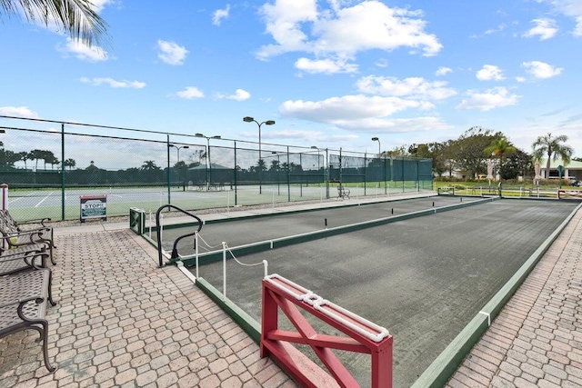 view of property's community featuring a tennis court and fence