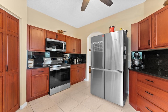 kitchen with appliances with stainless steel finishes, tasteful backsplash, dark stone countertops, and light tile patterned flooring