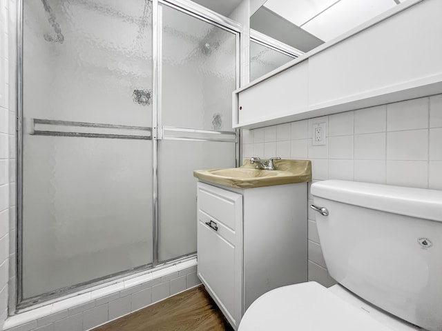 bathroom with tile walls, decorative backsplash, toilet, a stall shower, and wood finished floors