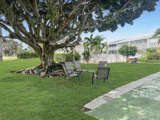 view of property's community with shuffleboard, a yard, and fence