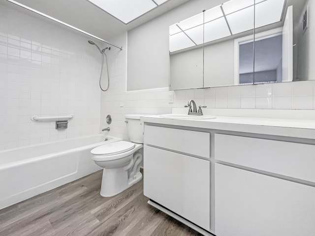 full bath with toilet, vanity, wood finished floors, shower / bathtub combination, and tile walls