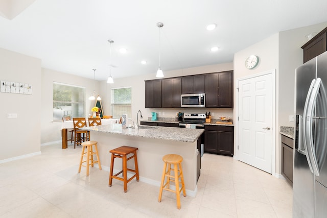 kitchen featuring stainless steel appliances, a breakfast bar area, dark brown cabinets, a kitchen island with sink, and pendant lighting