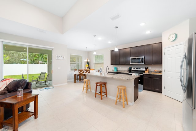 kitchen with hanging light fixtures, a kitchen island with sink, a kitchen breakfast bar, dark brown cabinets, and appliances with stainless steel finishes