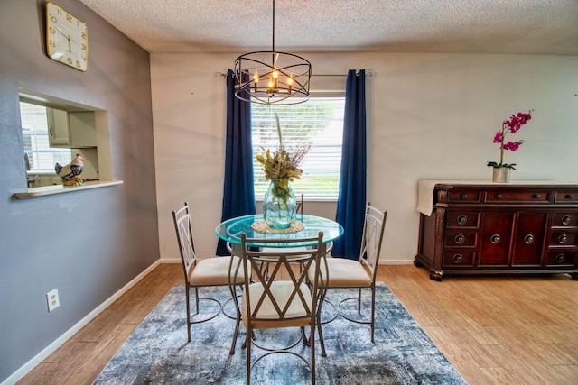 dining space with an inviting chandelier, a textured ceiling, and light hardwood / wood-style flooring