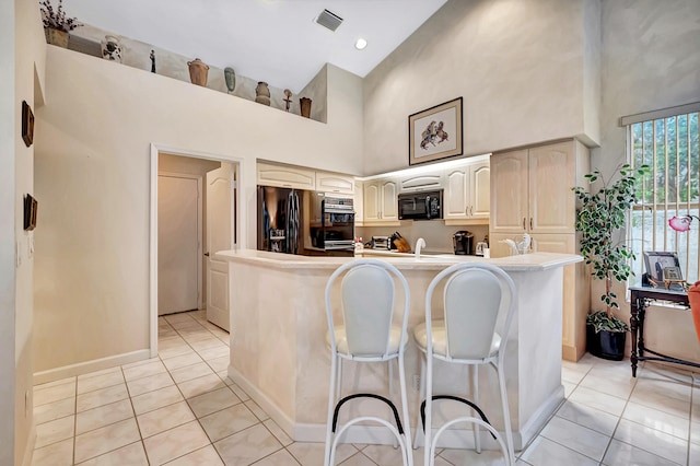 kitchen featuring a breakfast bar, a center island with sink, stainless steel fridge, a towering ceiling, and light tile patterned flooring