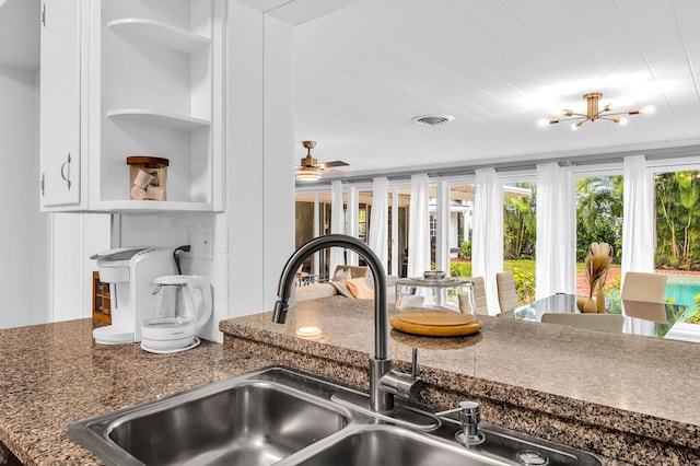 details featuring dark stone counters, sink, and ceiling fan with notable chandelier