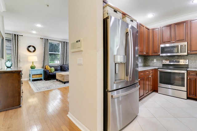 kitchen with stainless steel appliances, decorative backsplash, crown molding, light stone countertops, and light hardwood / wood-style flooring