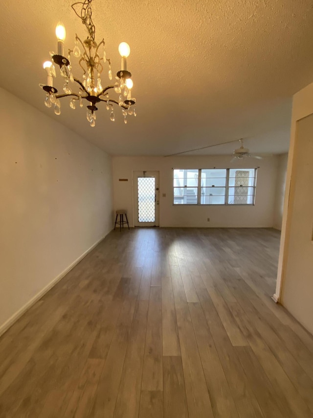 unfurnished living room with hardwood / wood-style floors, ceiling fan with notable chandelier, and a textured ceiling