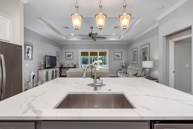 kitchen featuring light stone counters, crown molding, sink, pendant lighting, and an island with sink