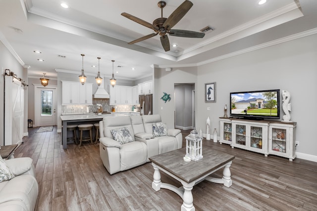 living room with ceiling fan, a barn door, crown molding, light hardwood / wood-style floors, and a tray ceiling