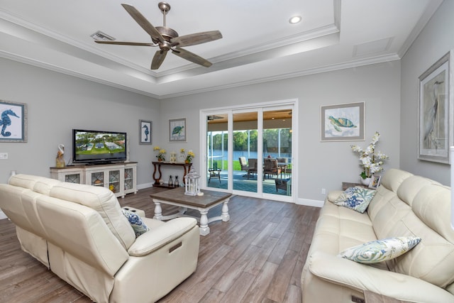 living room featuring ceiling fan, a raised ceiling, light wood-type flooring, and crown molding