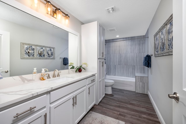 full bathroom with a textured ceiling, vanity, hardwood / wood-style flooring, toilet, and tiled shower / bath