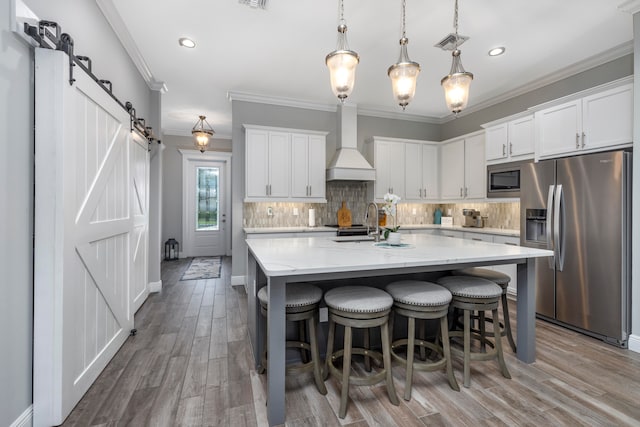 kitchen with custom exhaust hood, stainless steel appliances, pendant lighting, a barn door, and white cabinetry