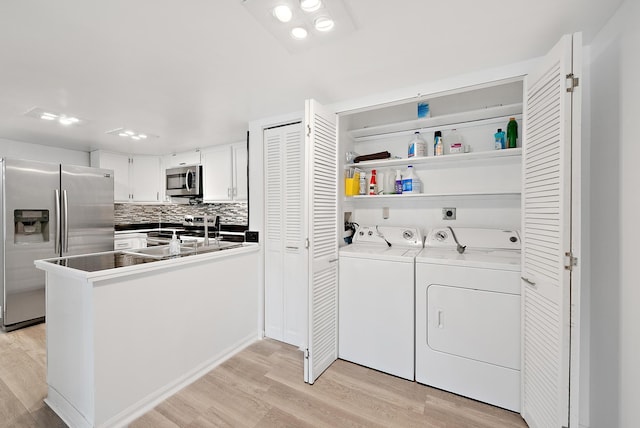 laundry area with light wood-type flooring, washing machine and dryer, and sink