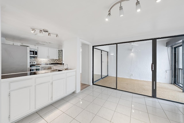 kitchen with stainless steel appliances, white cabinetry, sink, light tile patterned floors, and decorative backsplash