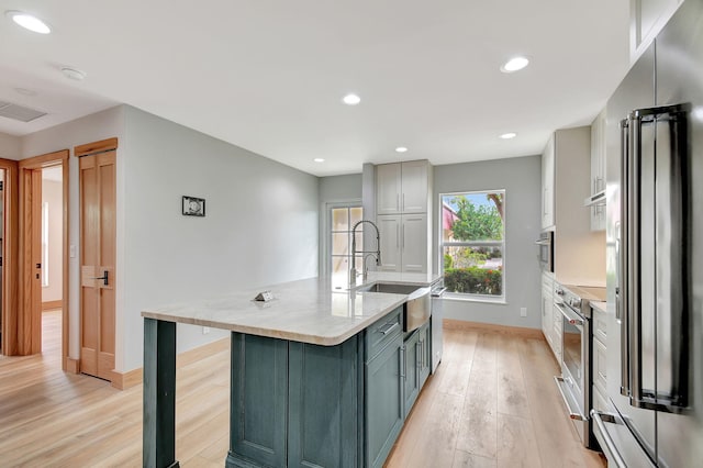 kitchen featuring light wood-type flooring, gray cabinets, a large island, and appliances with stainless steel finishes